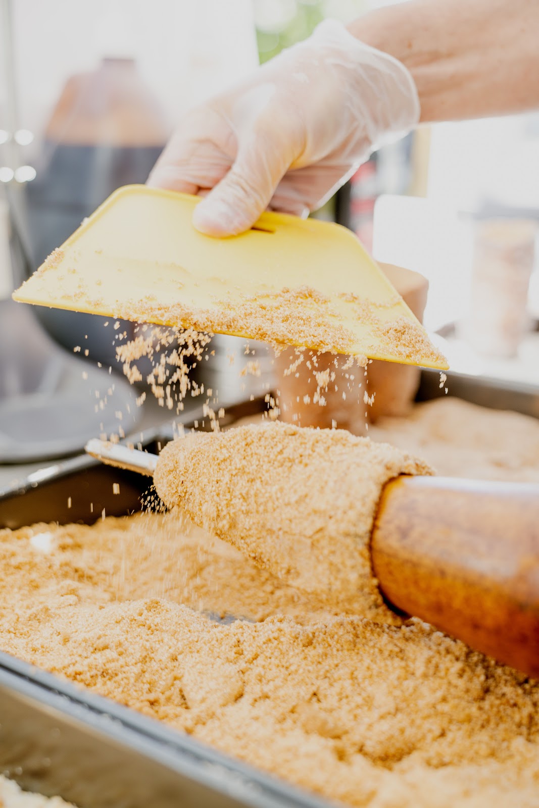 A gloved hand rolling chimney cake dough on a wooden roller through sugar crumb